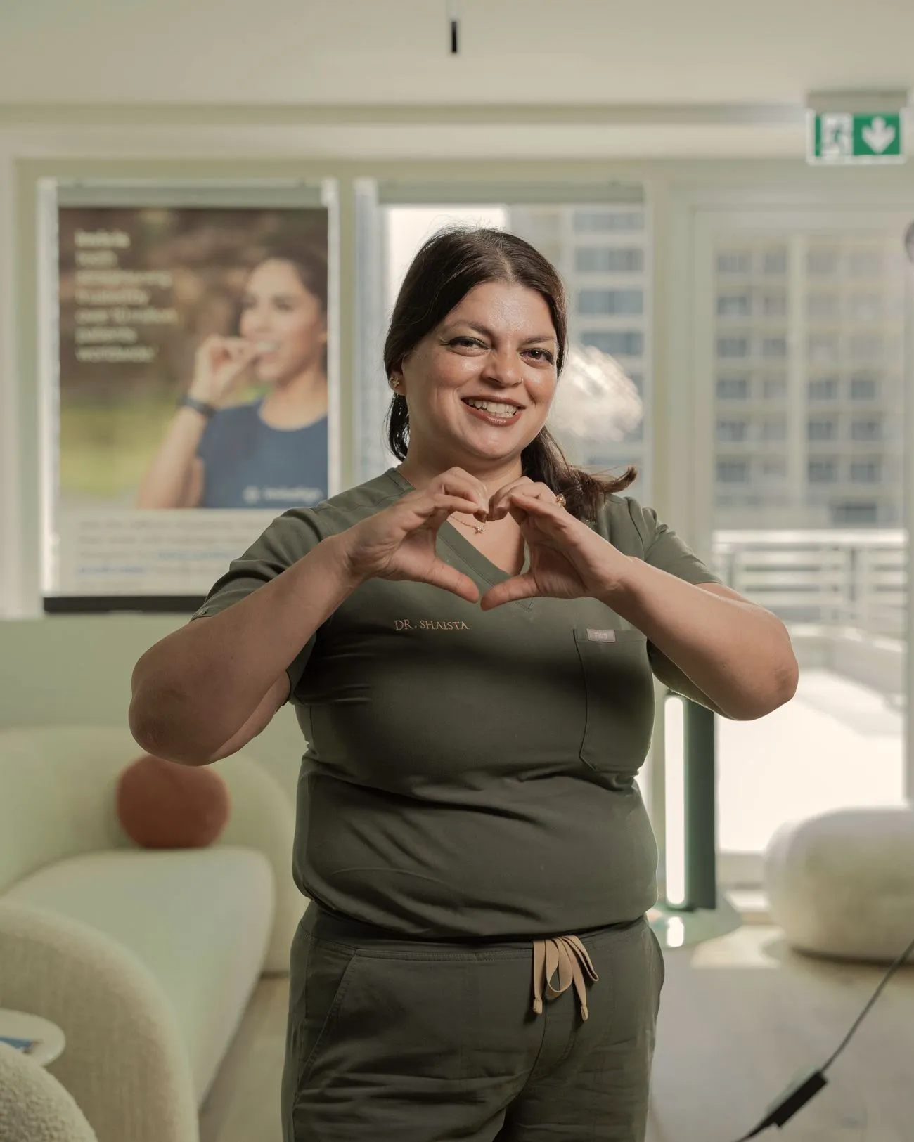 Dr Shaista Siddiqui, Medical Director of Hey Dental, smiling and making a heart shape with her hands